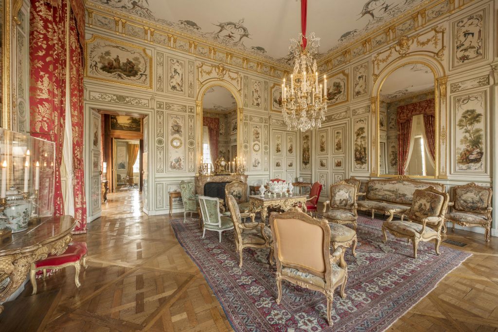 앤티크 가구, 샹들리에, 디테일한 벽 패널, 벽난로, 빨간 커튼이 있는 커다란 창문이 있는 화려한 객실.