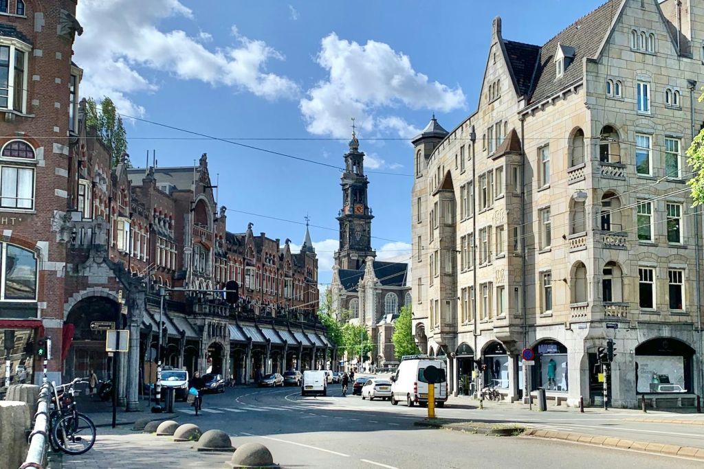 양쪽에 유서 깊은 벽돌 건물, 높은 시계탑을 배경으로 한 거리 풍경, 도로 위 차량.