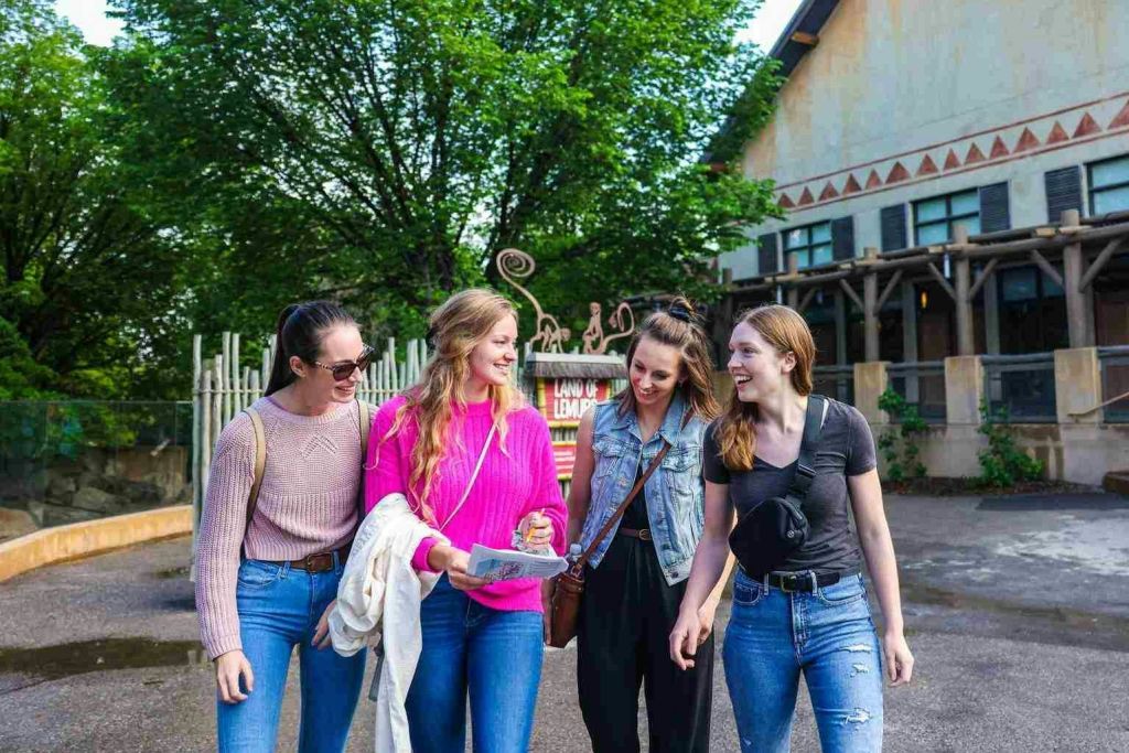 건물 밖에서 나무와 표지판을 배경으로 세 명의 여성이 미소를 짓고 걷고 있습니다. 하나는 지도를 들고 있습니다.