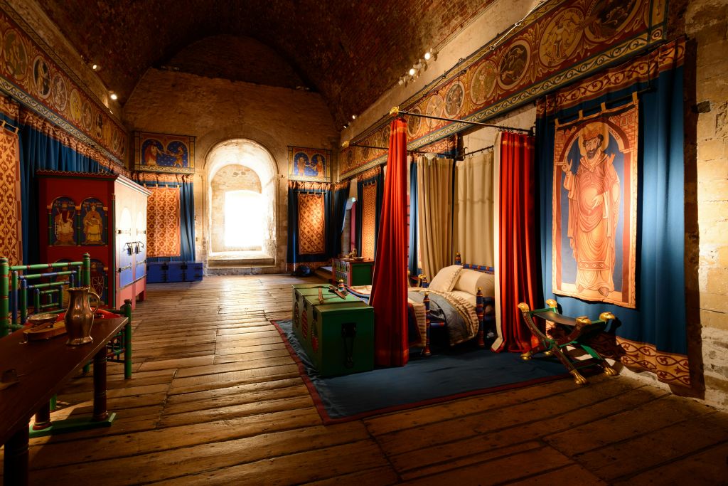 화려한 커튼, 태피스트리, 캐노피 침대, 중세 스타일의 가구로 장식된 나무 바닥의 역사적인 객실입니다.