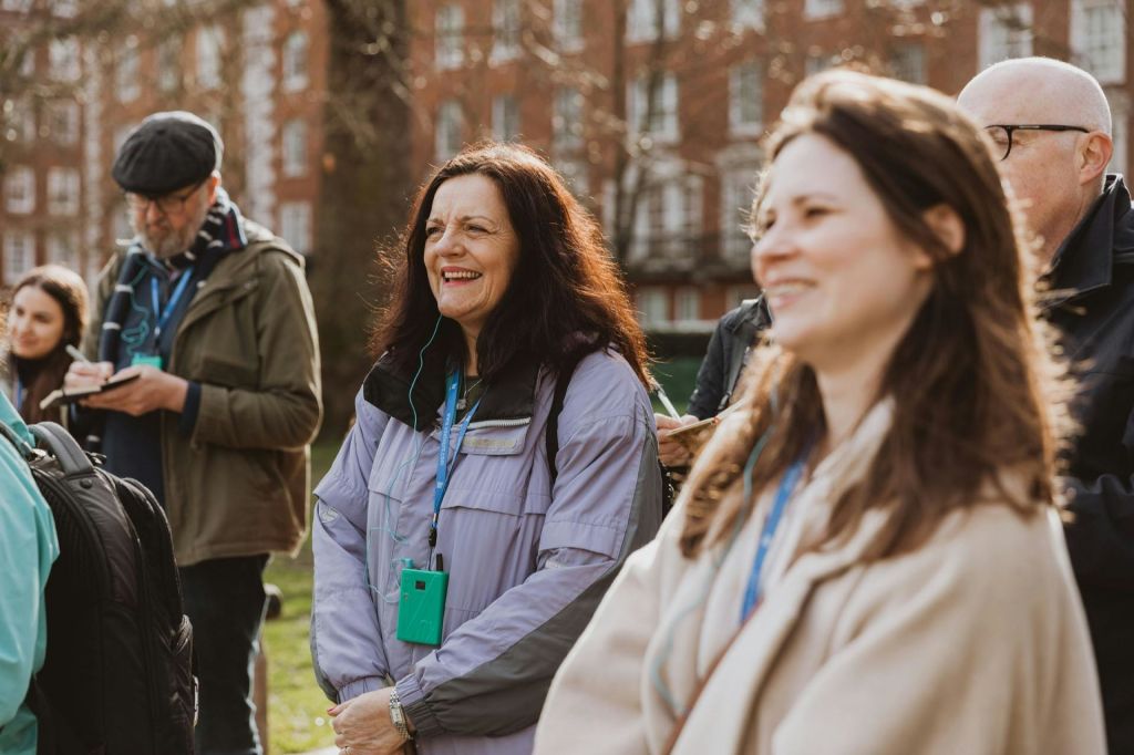 여러 사람이 밖에 서서 웃으며 방아끈을 매고 있습니다. 배경에는 나무와 복층 건물이 포함됩니다.