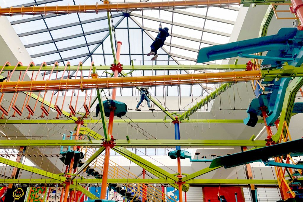 두 사람이 유리 천장이 있는 건물 내에 세워진 다양한 장애물이 있는 다채로운 실내 로프 코스를 항해합니다.