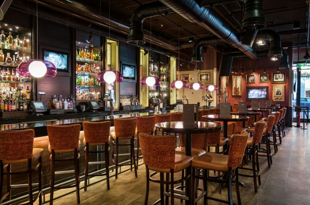 높은 고리 버들 의자, 원형 테이블, 구형 램프, 카운터 뒤의 다양한 병을 갖춘 세련된 바입니다.