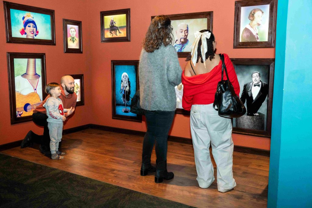성인 3명과 어린이 1명이 나무 바닥과 주황색 벽이 있는 미술관에서 독특한 초상화 그림을 보고 있습니다.