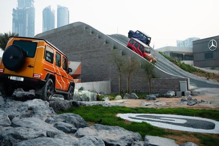 세 대의 SUV, 두 대는 하강하고 한 대는 콘크리트 경사로를 오르며, 바위와 건물을 배경으로 합니다.