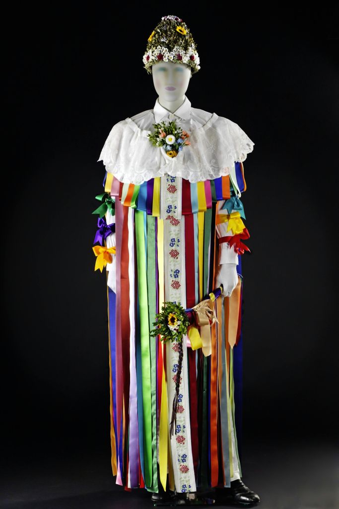 화려한 리본, 레이스 칼라, 꽃 액세서리, 장식된 헤드피스가 있는 전통 의상을 입은 마네킹입니다.