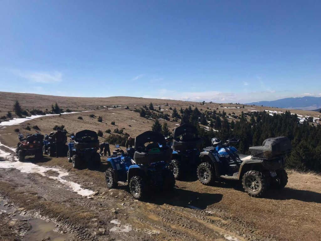 여러 대의 ATV가 맑고 푸른 하늘 아래 언덕에 주차되어 있으며, 일부 사람들은 그 근처에 모여 있고 나무를 배경으로 하고 있습니다.