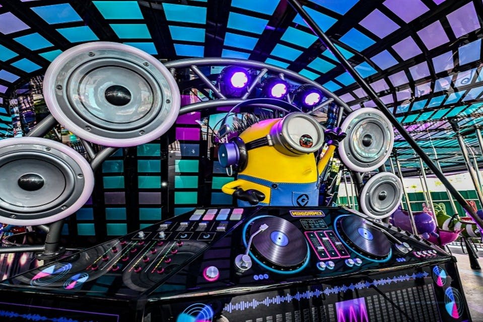 스피커와 조명으로 둘러싸인 DJ로 분장한 미니언 캐릭터가 다채로운 DJ 무대에 서 있습니다.