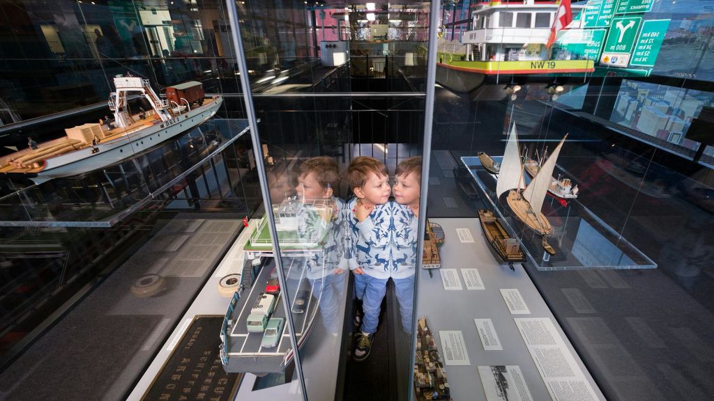 한 어린이가 해양 박물관 내 유리 케이스에 전시된 선박 모델을 바라보고 있습니다. 유리에 아이의 반사가 보입니다.