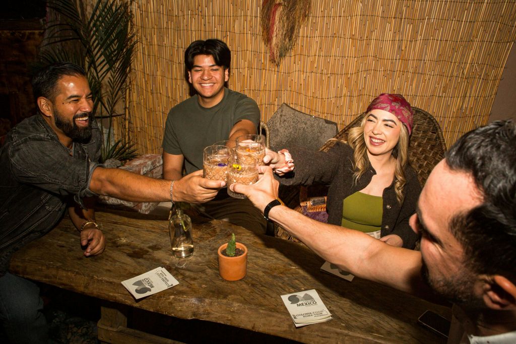 작은 선인장과 컵받침이 놓인 나무 테이블에서 네 명이 함께 미소를 짓고 잔을 찡그리고 있습니다.