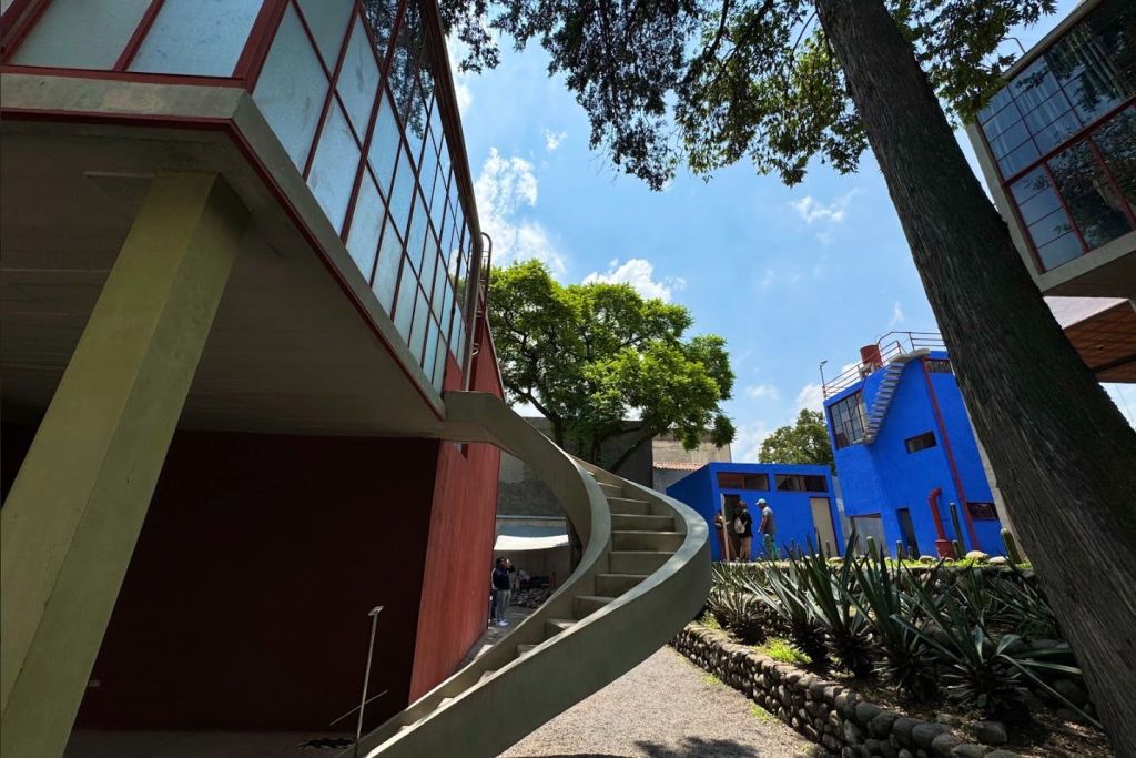 나무와 맑은 하늘을 배경으로 빨간색과 파란색 건물 옆의 곡선형 콘크리트 계단.