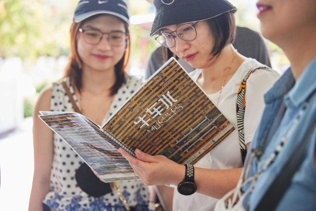 안경과 모자를 쓴 두 사람이 '워커' 라는 제목의 책자나 잡지를 흐릿하고 잎이 무성한 배경으로 바라보고 있습니다.