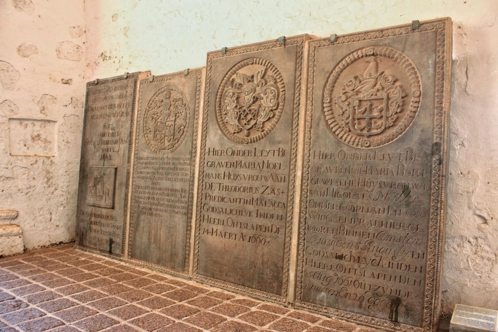 타일 바닥이 있는 역사적인 배경에 문장과 비문이 새겨진 돌판이 줄지어 있습니다.