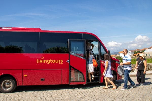 화창한 날 '리빙투어' 라고 적힌 빨간색 투어 버스에 탑승하는 사람들.