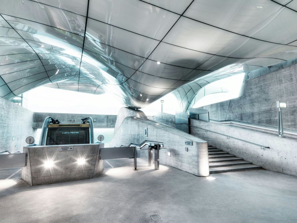 세련되고 반사되는 천장, 콘크리트 벽, 사람, 에스컬레이터, 계단, 개찰구가 없는 현대적이고 미래지향적인 실내 공간.