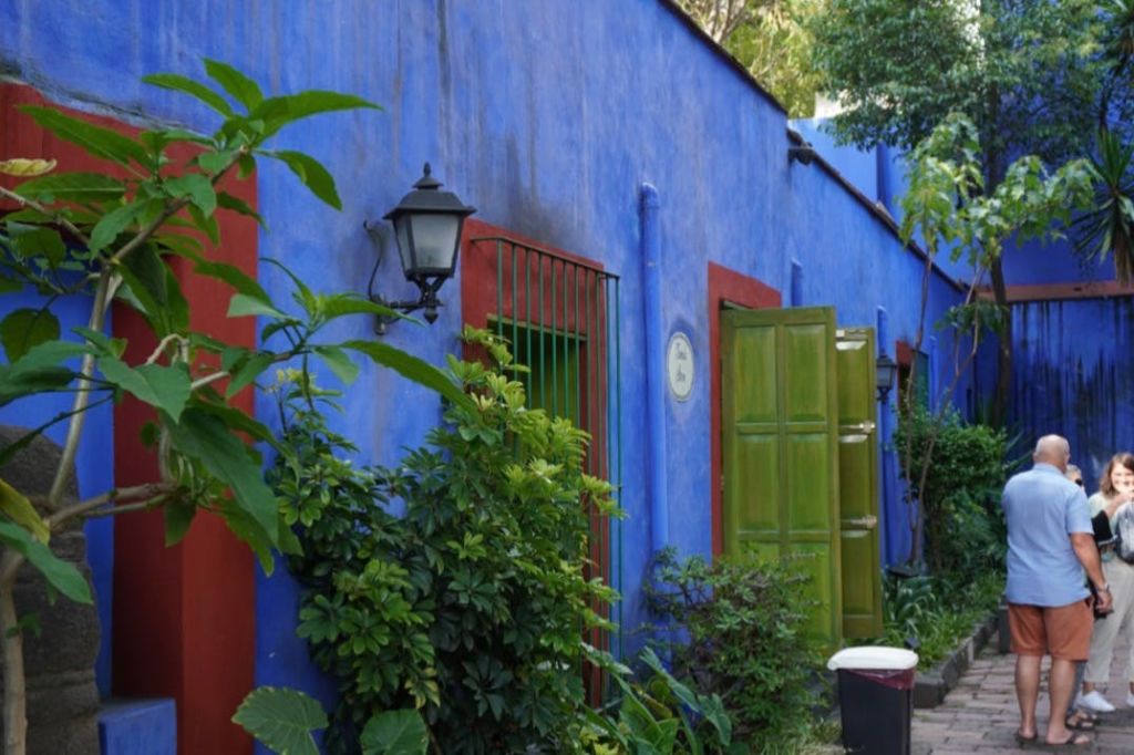 푸른 문과 창문이 있는 파란색과 빨간색 건물 외관은 울창한 단풍과 야외 등불로 둘러싸여 있습니다.