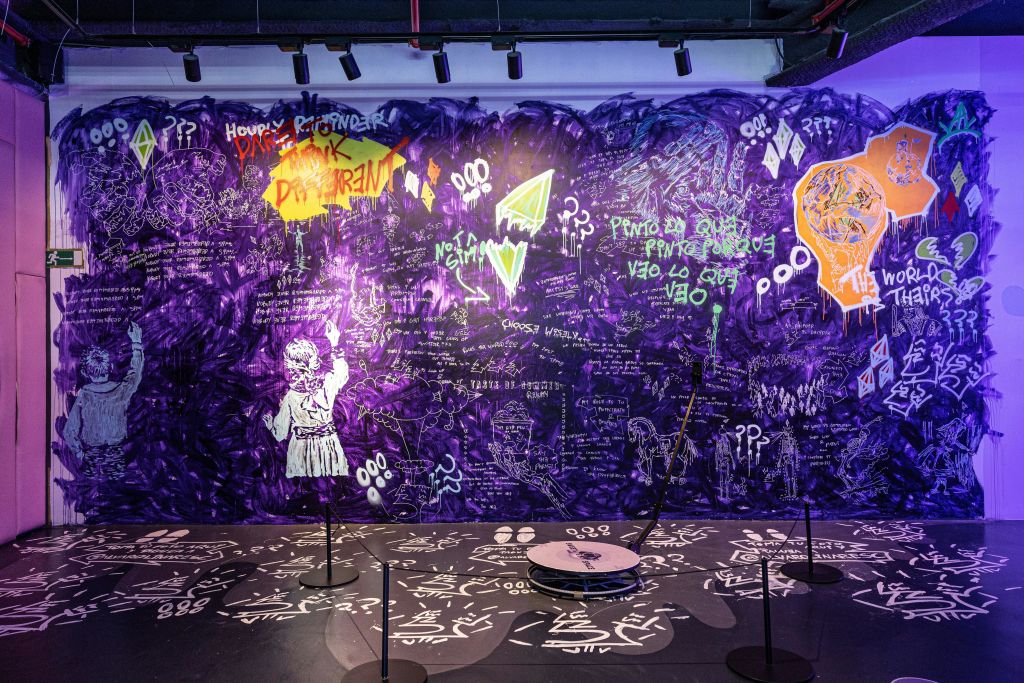 보라색 배경에 네온 그래피티가 그려진 벽화로, 그림과 텍스트가 특징입니다. 아이 같은 모습이 왼쪽에 흰색으로 칠해져 있다.