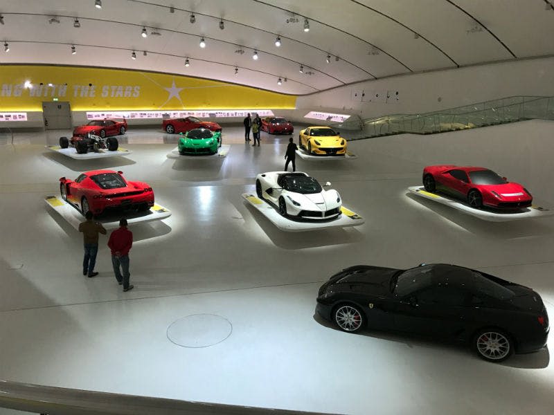 빨간색, 녹색, 흰색, 노란색, 검은색 모델 등 다양한 스포츠카를 전시하는 전시실로, 몇 명이 함께 관람합니다.