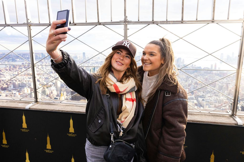 도시 풍경을 배경으로 야외 전망대에서 셀카를 찍는 두 여성.