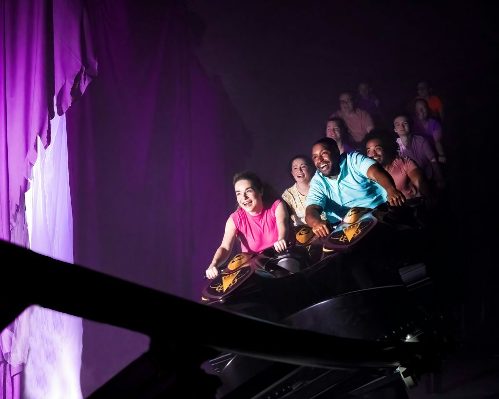 조명이 어두운 환경에서 롤러코스터를 타며 웃는 사람들.