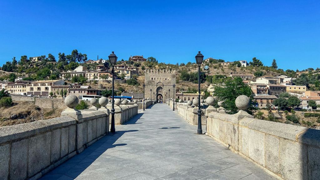 가로등이 있는 돌다리는 흩어진 건물과 맑고 푸른 하늘이 있는 언덕에 세워진 역사적인 게이트하우스로 이어집니다.