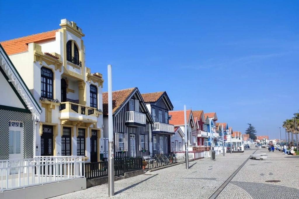 줄무늬 외관과 발코니가 있는 다채로운 주택이 맑고 푸른 하늘 아래 자갈길에 늘어서 있습니다.