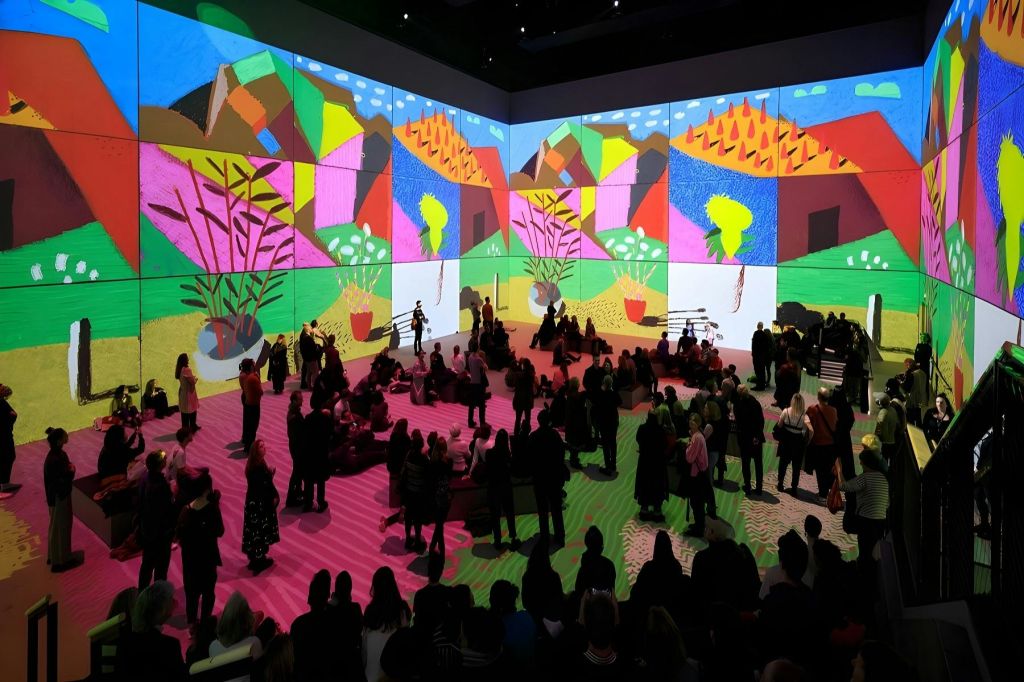 많은 사람들이 생생한 풍경과 추상적인 패턴을 특징으로 벽에 화려한 예술 투영을 관찰합니다.