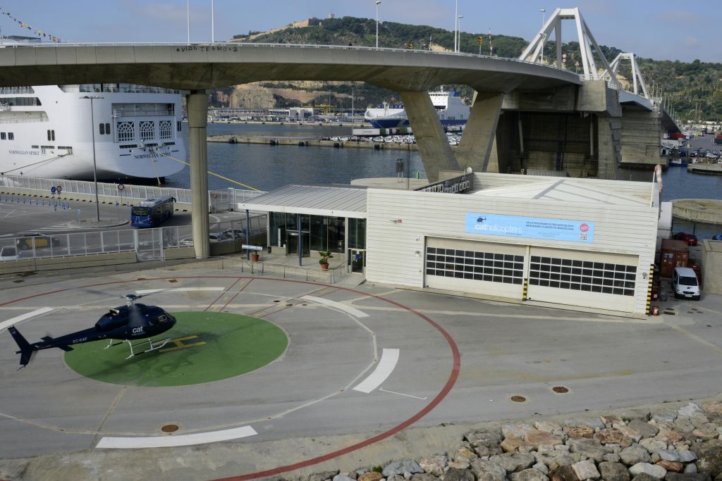 다리와 대형 선박을 배경으로 항구의 건물 옆에 있는 헬리콥터 착륙장.