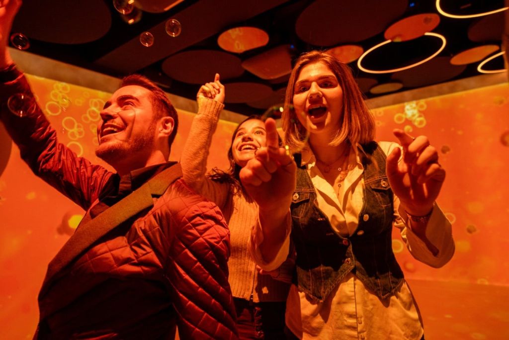 원형 천장 장식으로 활기차고 따뜻하게 빛나는 실내 환경에서 세 사람이 거품과 즐겁게 상호 작용합니다.