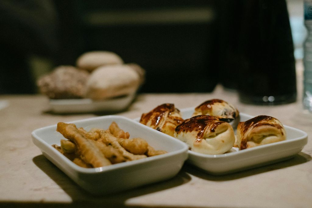 테이블 위에 음식 두 쟁반이 놓여 있습니다. 하나는 튀긴 음식이고, 다른 하나는 페이스트리입니다. 배경이 흐릿하면 빵이 더 많아집니다.