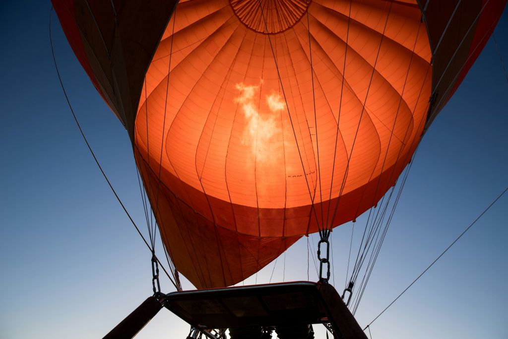 맑고 푸른 하늘을 배경으로 햇살이 비추는 주황색 천을 강조하는 열기구 아래쪽의 풍경.