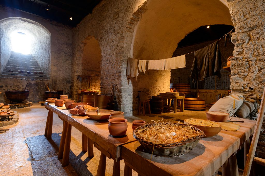 돌담, 나무 테이블, 도자기, 음식 바구니, 마른 천이 걸려 있는 소박한 주방입니다.