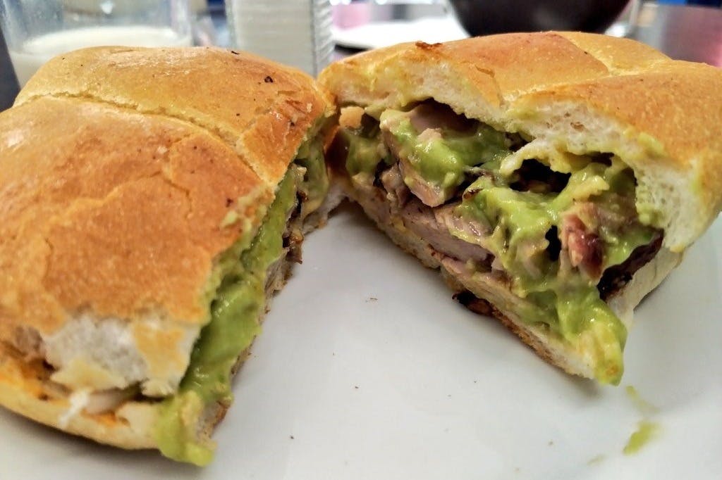 구운 고기와 크리미한 아보카도를 반으로 자른 갓 만든 토르타를 흰색 접시에 담아 클로즈업합니다.