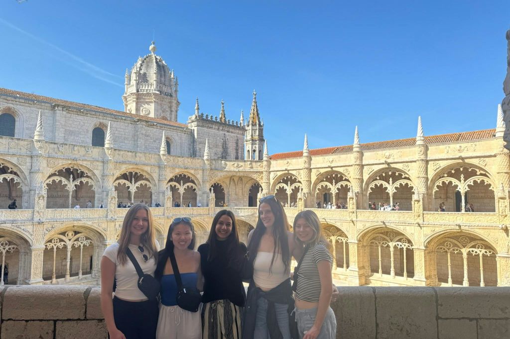 맑고 푸른 하늘 아래 아치와 탑이 있는 화려한 건물 앞에 5명이 서 있습니다.