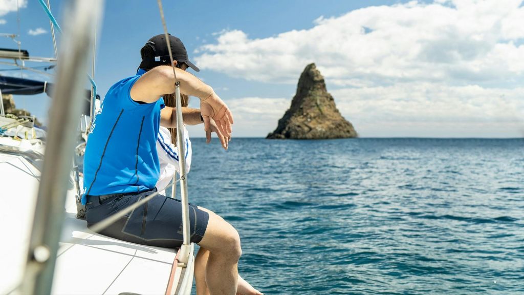 보트에 앉아 부분적으로 흐린 푸른 하늘 아래 바다의 먼 바위 지층을 바라보는 두 사람.