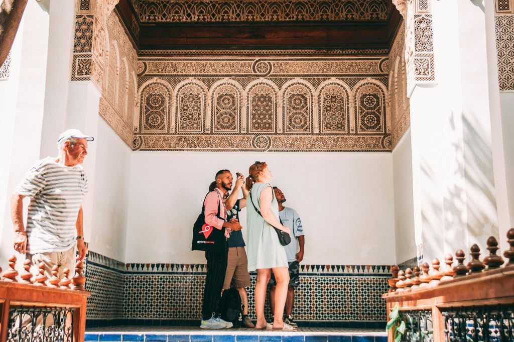 정교한 타일 작업과 화려한 패턴으로 꾸며진 방 안에 서 있는 한 무리의 사람들이 디테일을 살펴보고 있습니다.