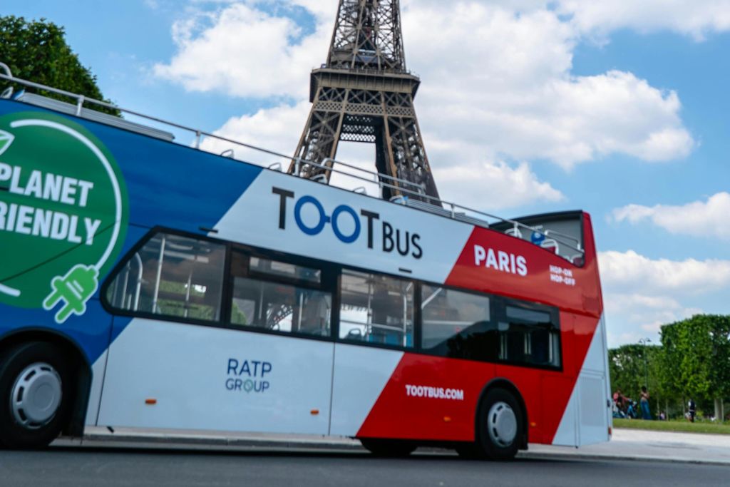 부분적으로 흐린 하늘을 배경으로 에펠탑이 있는 "TOOTBus Paris" 라는 이름의 2층 투어 버스가 있습니다.