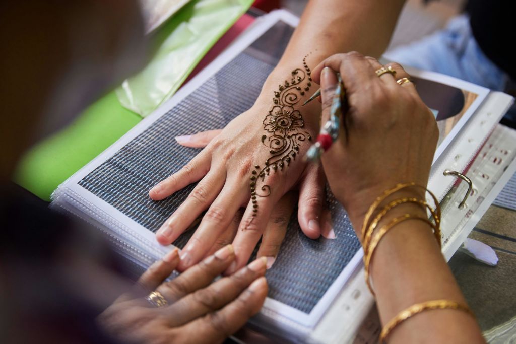 한 사람이 꽃과 복잡한 패턴이 보이는 다른 사람의 손에 디테일한 헤나 디자인을 적용하고 있습니다.