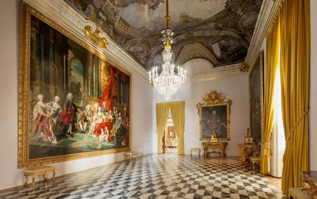 대형 샹들리에, 벽에 바로크 그림, 화려한 금색 가구, 체크무늬 대리석 바닥이 있는 고급스러운 객실입니다.