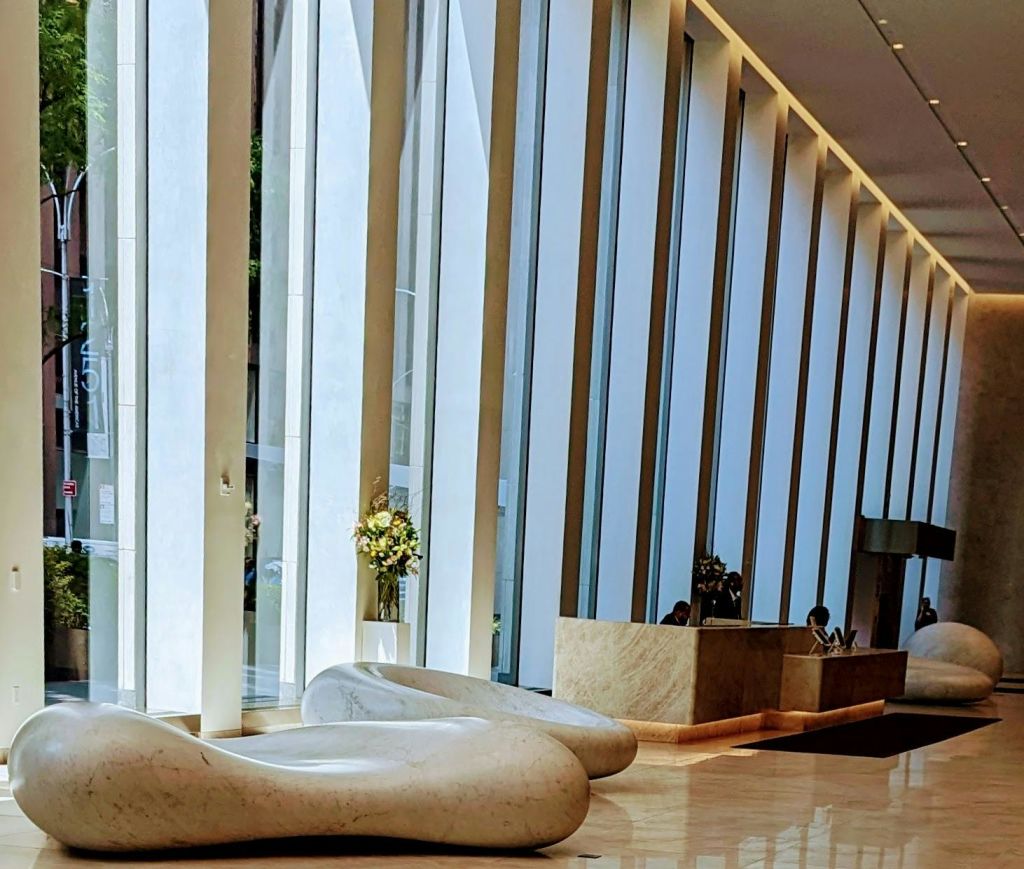 높은 창문, 추상적인 좌석, 프런트 데스크가 있는 현대적인 로비. 자연광이 광택이 나는 바닥을 비춥니다.