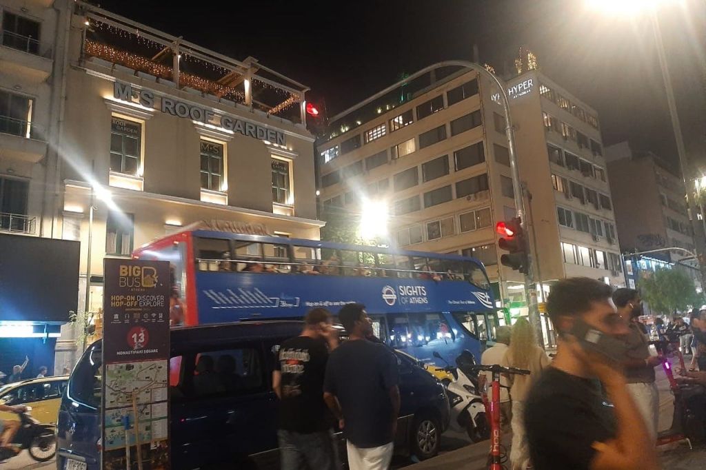 도시에서 밤에 2층 투어 버스 근처를 걷는 사람들. 건물과 조명이 배경으로 보입니다.