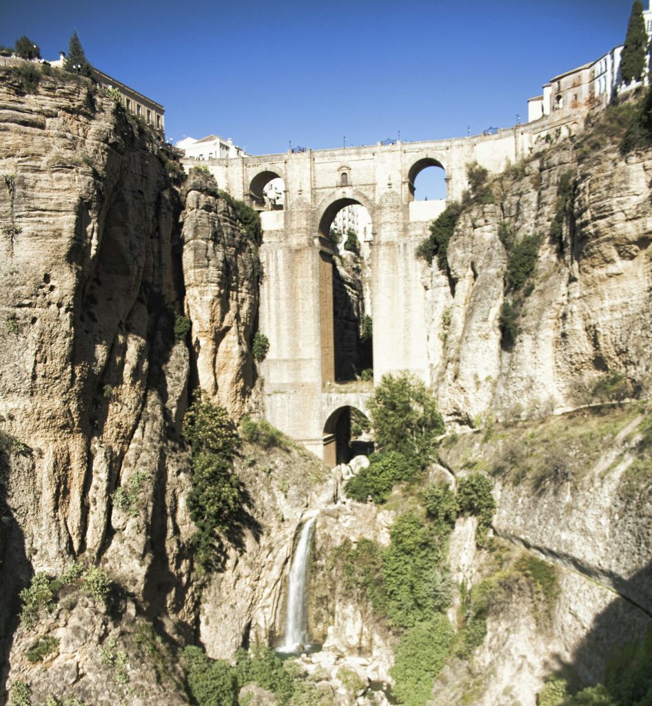 폭포가 있는 깊은 협곡 위로 3개의 아치형 스톤 브리지가 있습니다. 협곡 꼭대기에는 건물들이 줄지어 있습니다. 맑고 푸른 하늘.