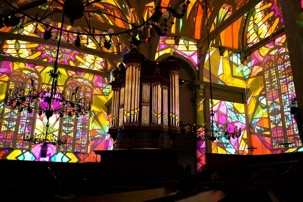 벽과 천장에 화려한 조명 무늬를 시전하는 스테인드글라스 창문이 있는 교회 내부의 대형 파이프 오르간.