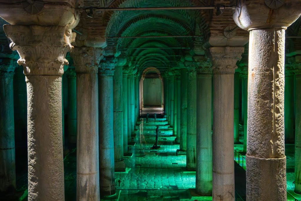 녹색 빛으로 빛나는 높은 기둥이 있는 고대 지하 수조는 바닥에 얕은 물을 반사합니다.