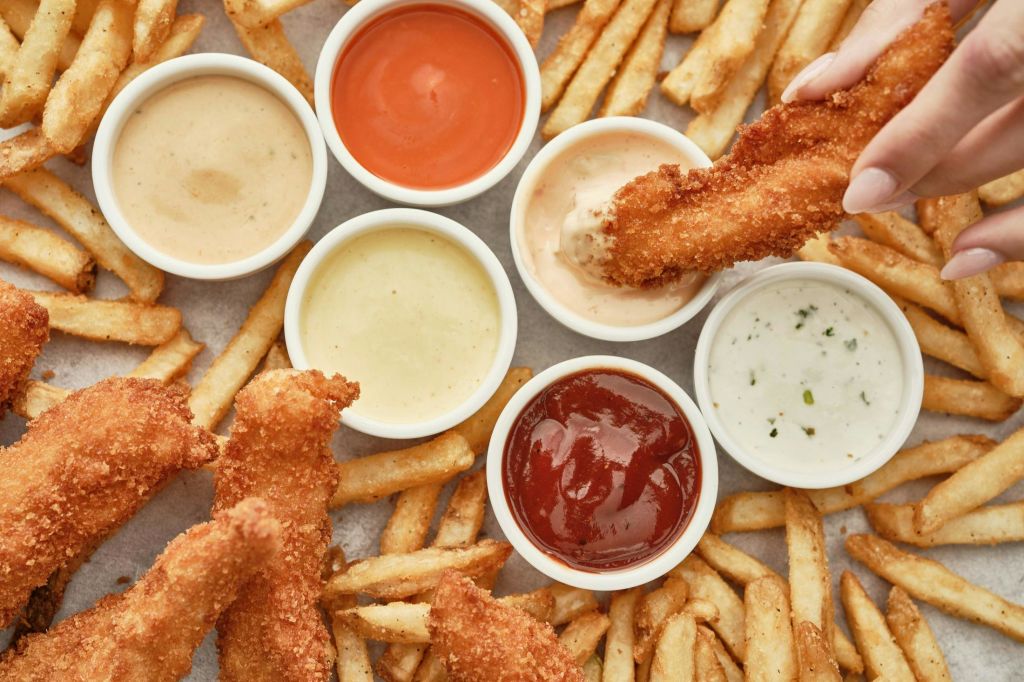 바삭한 치킨 텐더와 감자튀김, 다양한 디핑 소스가 표면에 배열되어 있습니다.
