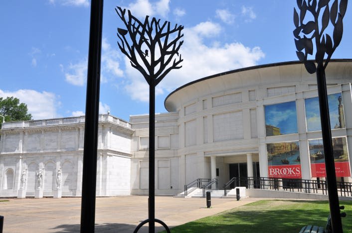 부분적으로 흐린 하늘 아래 커다란 흰색 박물관 건물 앞에 있는 나무의 현대적인 조각입니다.