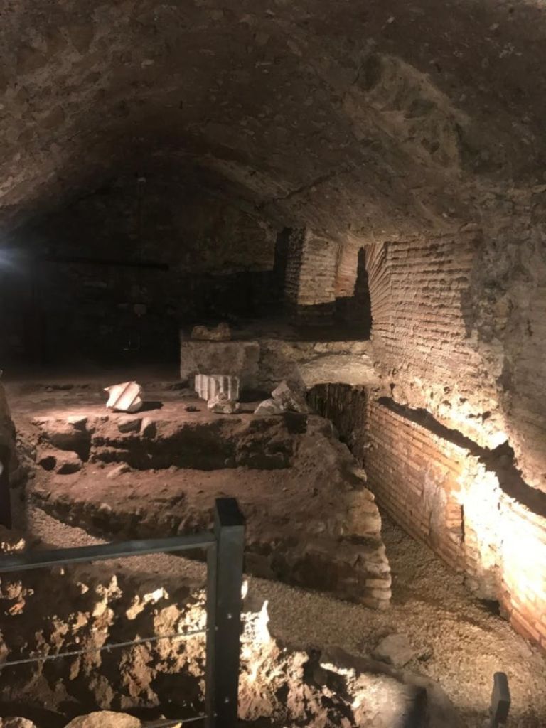 벽돌 벽과 석조 잔해가 있는 고대 지하 유적은 거친 질감을 강조하는 스포트라이트로 희미하게 빛납니다.