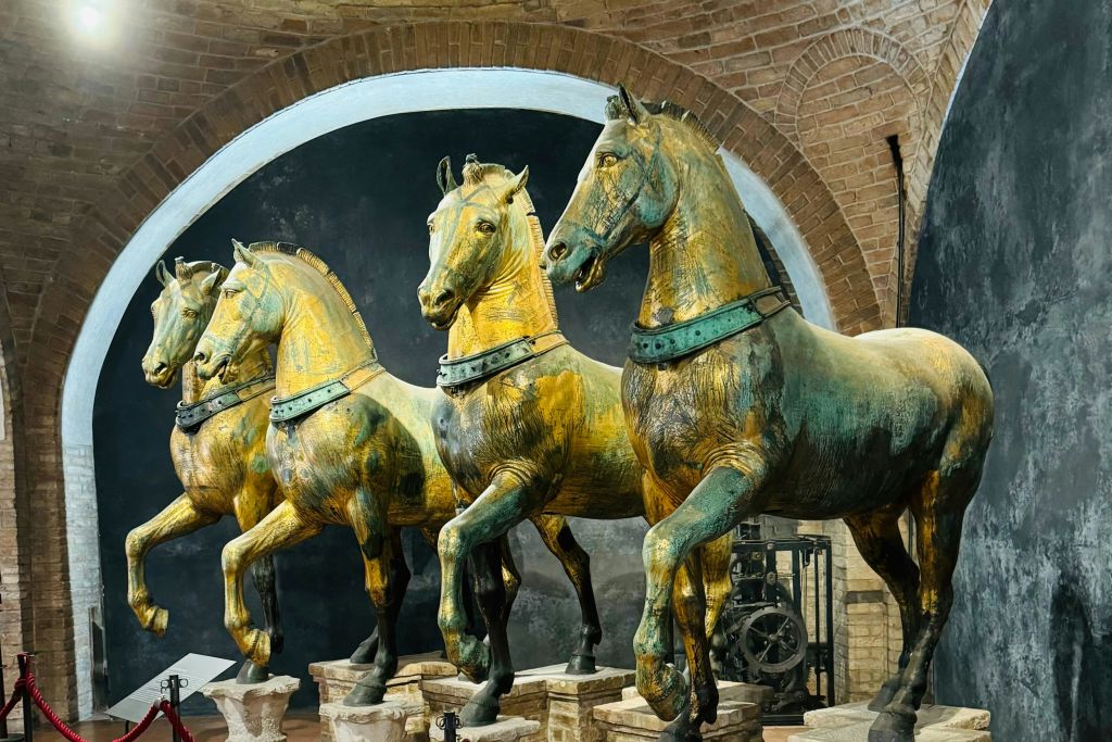 박물관 배경에 아치형 벽돌 배경과 둥근 어두운 패널이 있는 4개의 청동 말 조각상이 전시되어 있습니다.
