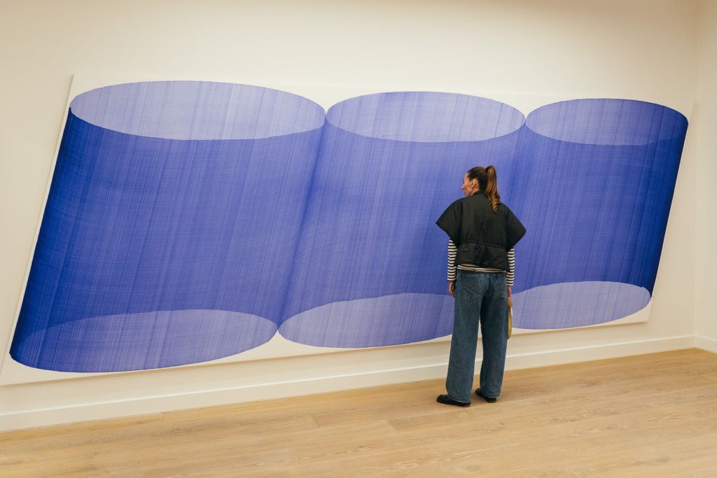 벽에 파란색으로 겹쳐진 원통형 모양을 묘사한 대형 작품 앞에 한 사람이 서 있습니다.