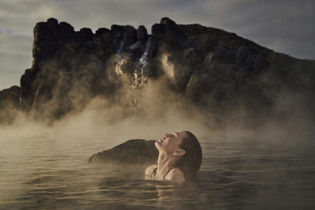 한 사람이 바위 폭포와 안개를 배경으로 찜질방 온천에서 휴식을 취하고 있습니다.